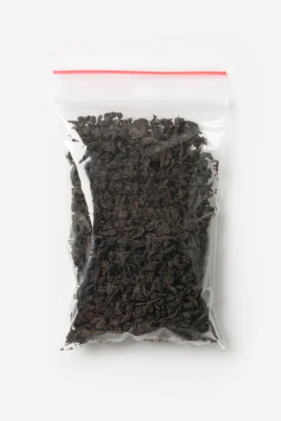 Sac à fermeture à glissière transparent en plastique avec plein de thé noir isolé sur blanc, modèle d'emballage sous vide avec clip rouge. Concept — Photo