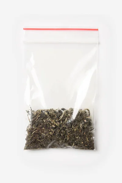 Plastic transparent zipper bag with a little dry green tea isolated on white, Vacuum package mockup with red clip. Concept. — Stock Photo, Image