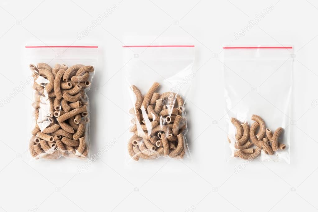 Set of three EMPTY, HALF AND FULL Plastic transparent zipper bag with wholegrain raw pasta isolated on white. Vacuum package mockup with red clip. Concept.