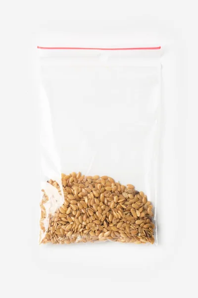 Пластиковый прозрачный пакет-молния с немного цельнозерновой муки сырые семена льна хлопьев изолированы на белом, вакуумная упаковка макет с красным зажимом. Концепция . — стоковое фото