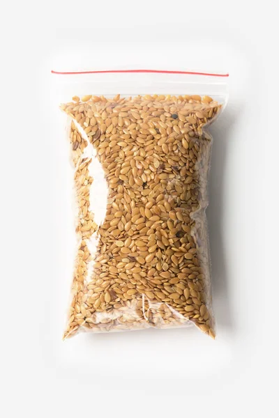 Saco de zíper transparente de plástico com sementes de linho cru completo cereal isolado no branco, pacote de vácuo mockup com clipe vermelho. Conceito . — Fotografia de Stock
