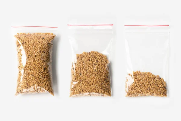 Conjunto de três EMPTY, HALF E FULL plástico saco de zíper transparente com sementes de linho cru cereal isolado em branco. Pacote de vácuo mockup com clipe vermelho. Conceito . — Fotografia de Stock