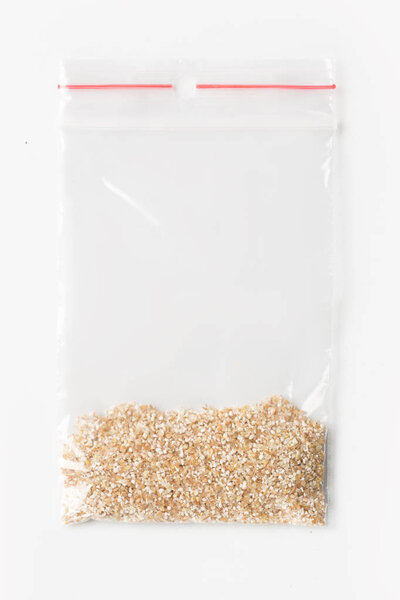 Пластиковые прозрачные молнии мешок с небольшим количеством сырой пшеничной крупы изолированы на белом, Вакуумный пакет макет с красным зажимом. Концепция
.