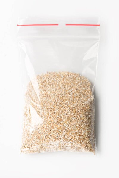 Пластиковые прозрачные молнии мешок с половиной сырой пшеничной крупы изолированы на белом, Вакуумный пакет макет с красным зажимом. Концепция
