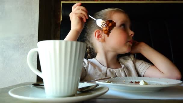 Flicka vid bordet dricka te och äta tårta från en tallrik — Stockvideo