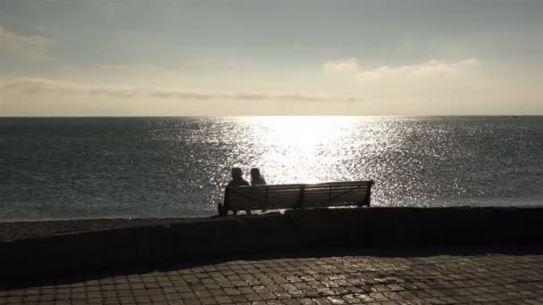 Pár ember ül egy padon, a nap vagy az óceánra néző — Stock videók