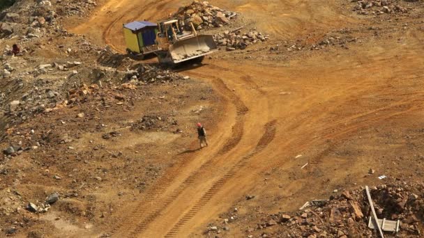 Travailleur dans le casque va sur un chemin de terre indiquant la façon dont le bulldozer — Video