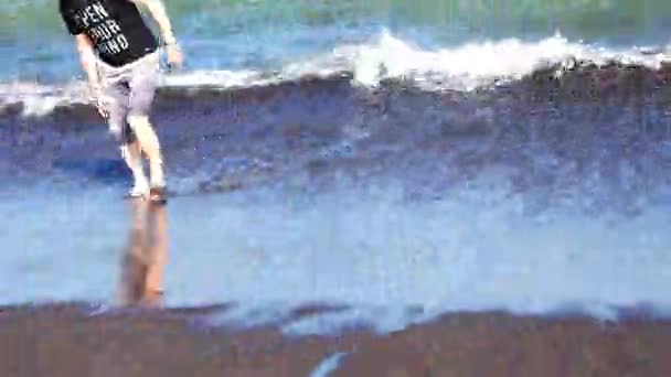Człowiek boso idzie na czarnej piaszczystej zimno ocean woda — Wideo stockowe