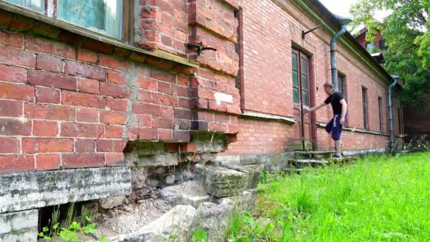 Der Tourist begutachtet die Veranda und blickt in die Fenster eines alten, historischen einstöckigen Gebäudes aus Ziegelsteinen — Stockvideo