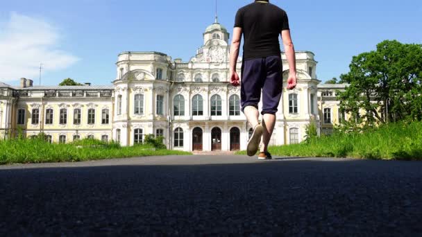 Mężczyzna wychodzi z klatki i spacery wzdłuż drogi w kierunku zabytkowego zamku — Wideo stockowe