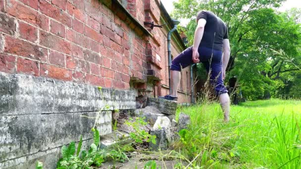 Un hombre en forma atlética estudia el terreno de un castillo histórico abandonado de una casa de ladrillo — Vídeo de stock