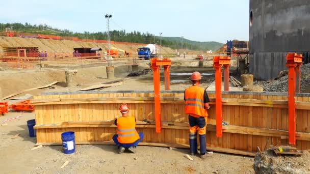 Werknemers in oranje uniform en helmen opgaand hout bekisting — Stockvideo