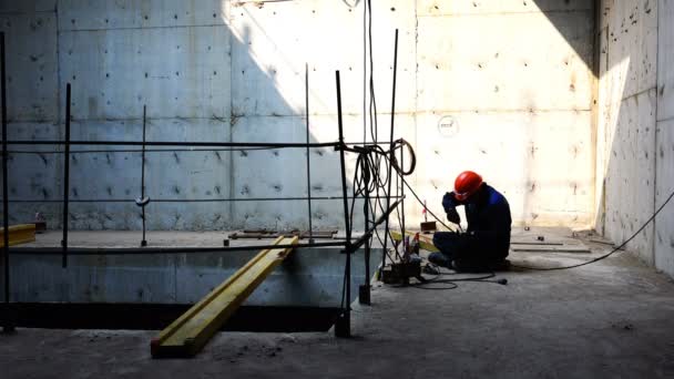 Trabajador en una bata y casco en un piso de hormigón realiza trabajos de instalación con hierro — Vídeos de Stock