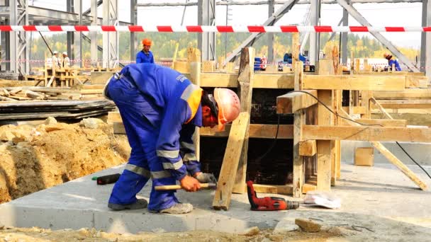 El constructor con una bata y casco asegura el apoyo para el encofrado de cimentación — Vídeo de stock