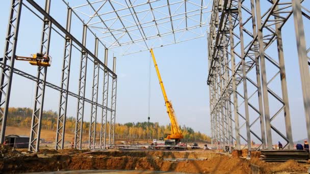 La grue travaille avec des charges sur le chantier sous les structures métalliques du bâtiment de la ferme — Video