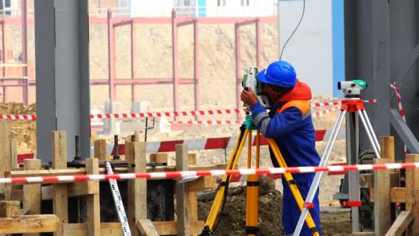 El topógrafo en el casco realiza mediciones en el nivel y el teodolito en el sitio de construcción — Vídeo de stock