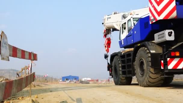 Movement of a self-propelled crane on wheels along a protective fence along a dirt road — Stock Video