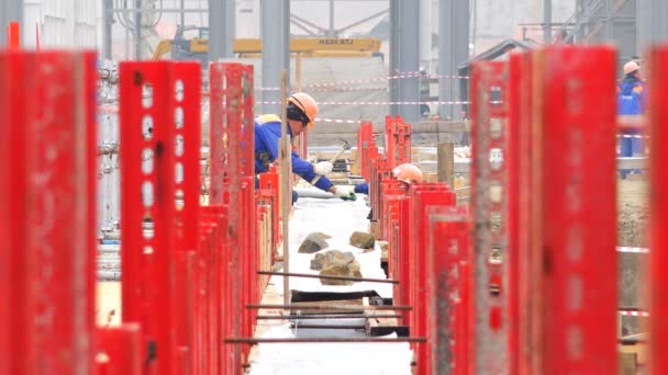 Trabajadores en cascos realizan trabajos de instalación sobre los cimientos — Vídeos de Stock