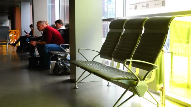 Пассажиры в аэропорту сидят в зале ожидания перед посадкой на самолет — стоковое видео