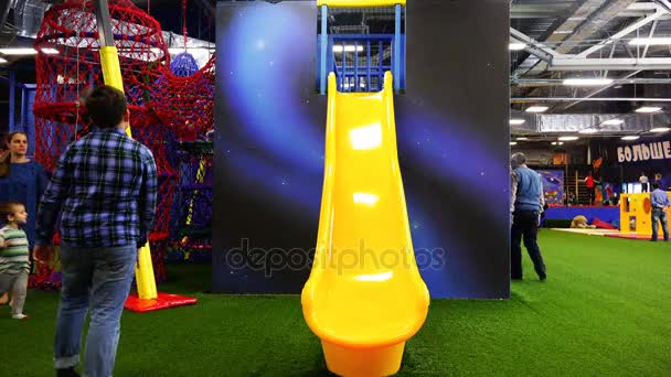 A criança desliza para baixo dos slides amarelos para os pais brincando no playground — Vídeo de Stock