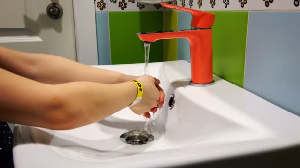 Ein Kind wäscht sich die Hände unter einem orangefarbenen Mixer — Stockvideo