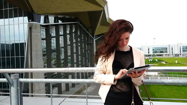 Mulher sexy em uma jaqueta usa tecnologias de TI perto da arquitetura elegante do edifício — Vídeo de Stock