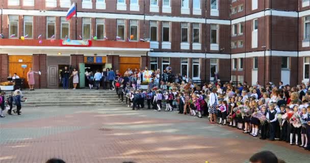 Leerlingen met boekentassen op hun schouders en bloemen in hun handen gaan op 1 september naar school — Stockvideo