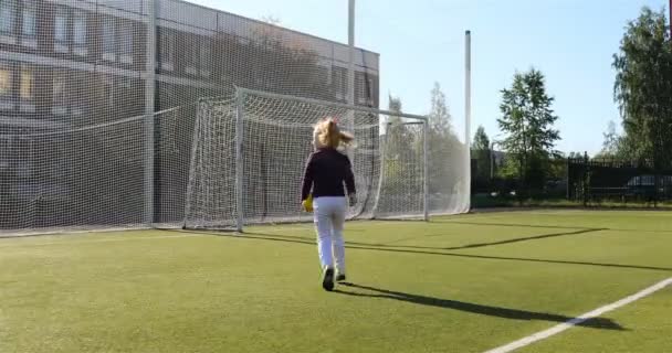 Uma menina corre em um campo de futebol com um brinquedo de pelúcia amarela em suas mãos — Vídeo de Stock