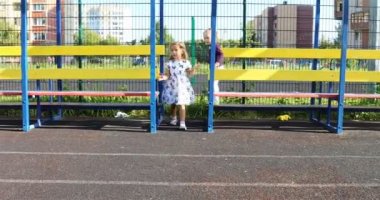 Üç ve dört yaşındaki kızlar güneşli havalarda bir spor stadyumunda oynuyorlar.