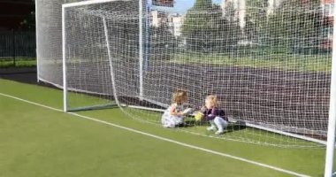 Küçük kızlar futbol kalesinin arkasındaki sahada yumuşak oyuncaklarla oynarlar.