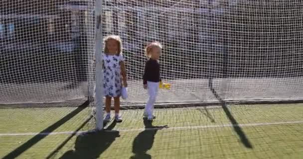 Duas meninas correr jogar e brincar em torno de um campo com uma superfície artificial verde — Vídeo de Stock