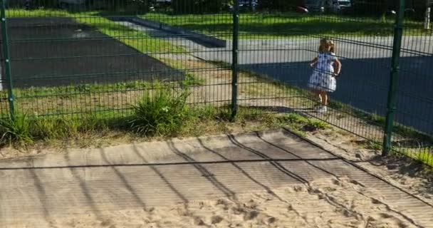 小さな女の子が庭の柵の外に出て晴れた日に散歩をしました — ストック動画