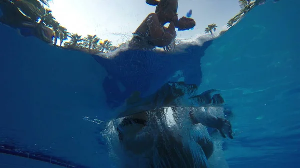 Bir kız ve bir oğlan su havuzuna atlayıp kameraya el sallıyorlar. Su altı ağır çekim