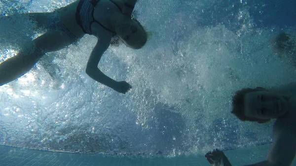 Bir erkek ve bir kız aynı anda havuza atlayıp yan tarafa tırmanıyorlar. Suyun altında çekim yapmak