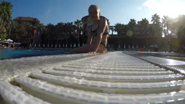 Une fille en maillot de bain est assise sur le bord de la piscine avec les pieds dans l'eau — Video