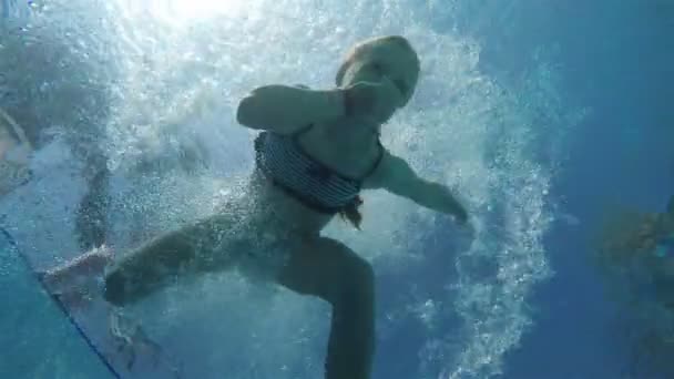O rapaz salta atrás da rapariga da beira da piscina. Tiro debaixo de água — Vídeo de Stock