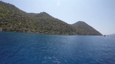 Bir deniz gemisi tepeli bir karanın kıyısına yelken açıyor.