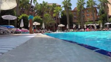 Bir Aqua aerobik hocası havuz kenarında ağzında bir ıslıkla dans eder ve ziyaretçileri canlandırır.