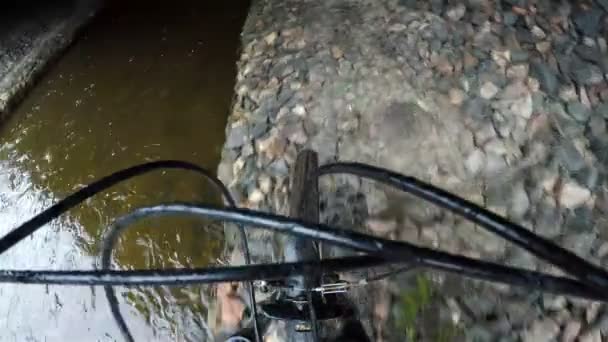 Un atleta rueda una bicicleta a lo largo de los gaviones a lo largo del arroyo bajo el puente — Vídeos de Stock