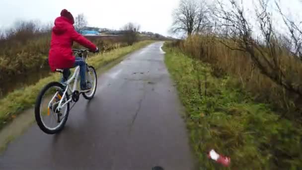 Una chica con una chaqueta roja monta una bicicleta blanca en un camino de asfalto — Vídeos de Stock