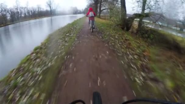 Два велосипедиста едут по грязной проселочной дороге у озера — стоковое видео