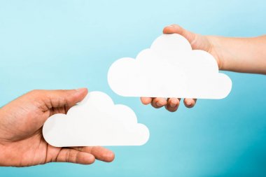 Two hands holding paper clouds on blue background. Cloud computing concept clipart