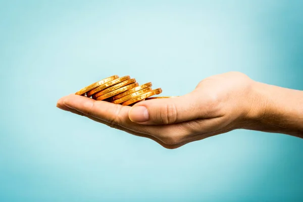 Hand hält goldene Münzen auf blauem Hintergrund. Geschäftskonzept — Stockfoto