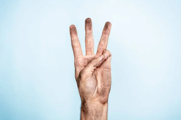 Чоловіча брудна рука, що показує три пальці на синьому фоні — стокове фото