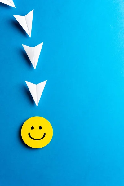 Sárga boldog arc, kék hátterű papírrepülőkkel. Társadalom — Stock Fotó