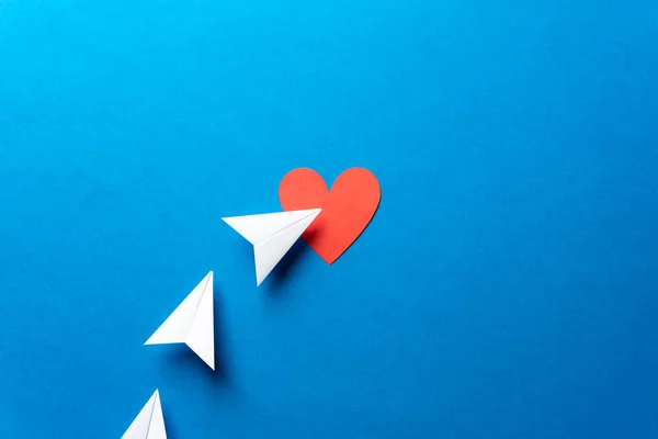 Three paper airplanes with red heart shape on blue background. S