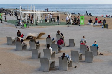 Barselona, İspanya. 14 Mart 2020. İspanya hükümetinin alarm durumuna geçmesine ve insanlardan evlerinde kalmalarını istemelerine rağmen, bulutlu bir cumartesi öğleden sonra Barselona sahilinde oturan kalabalık