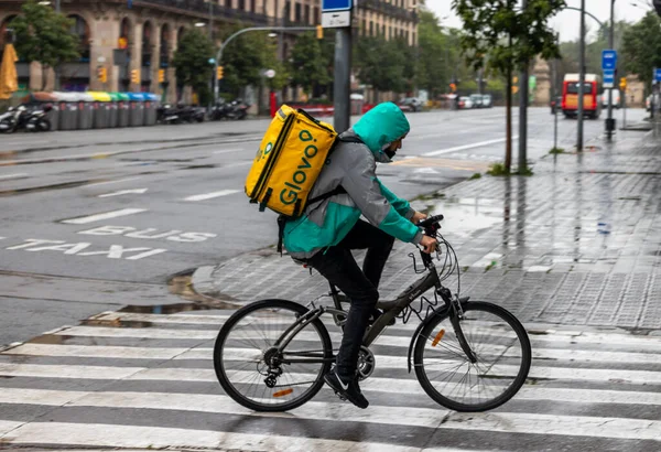 Barselona, İspanya. 20 Nisan, 2020. Glovo teslimatçısı yağmur altında Barcelona 'nın boş sokaklarında bisiklet sürüyor.