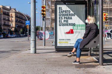 Barselona, İspanya. 24 Nisan 2020 'de. Barselona 'nın merkezinde otobüs bekleyen bir kadın. Covid salgını sırasında boş bir sokakta.