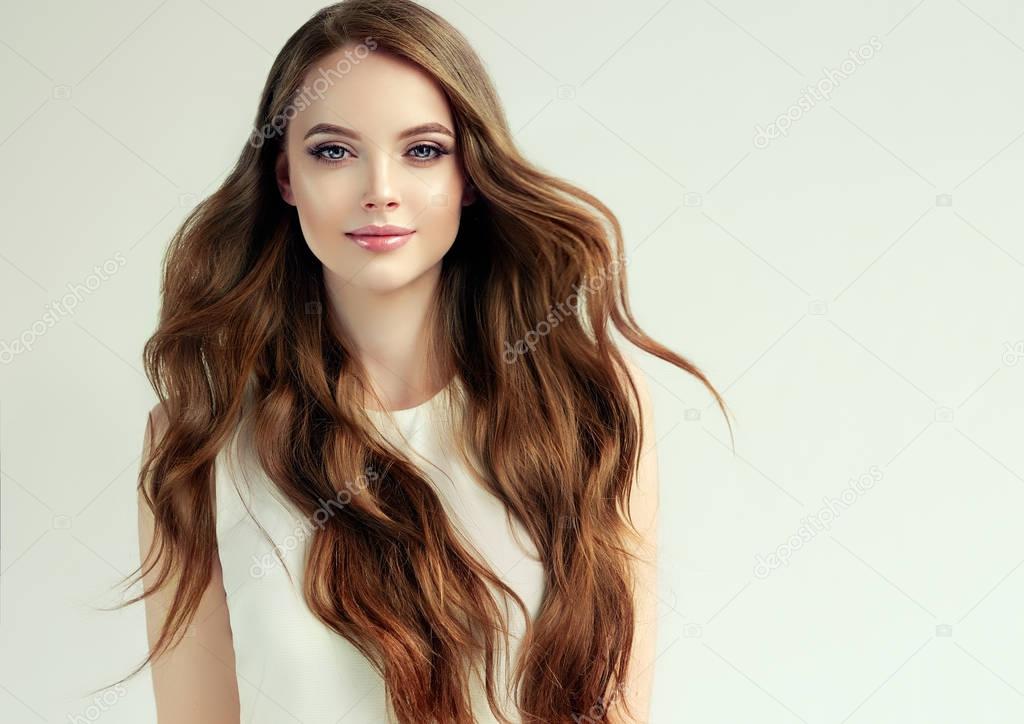 Brunette  girl with long  and   shiny ,wavy  hair .  Beautiful  model woman  with curly hairstyle   .Care and beauty of hair